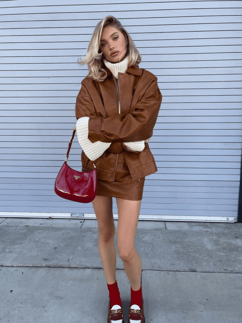 We continue to admire the beautiful and light out-of-season images of Elsa Hosk 🔥 The model is wearing a chic caramel set from the Lioness brand, consisting of a bomber jacket and a skirt. And how beautifully red accents in the form of a Prada bag, loafers, and socks go with it!