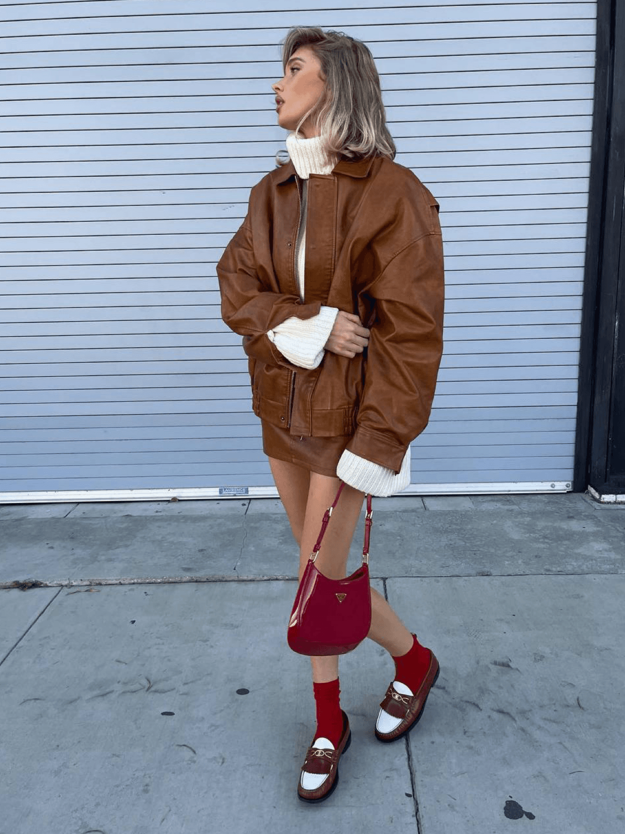 We continue to admire the beautiful and light out-of-season images of Elsa Hosk 🔥 The model is wearing a chic caramel set from the Lioness brand, consisting of a bomber jacket and a skirt. And how beautifully red accents in the form of a Prada bag, loafers, and socks go with it!